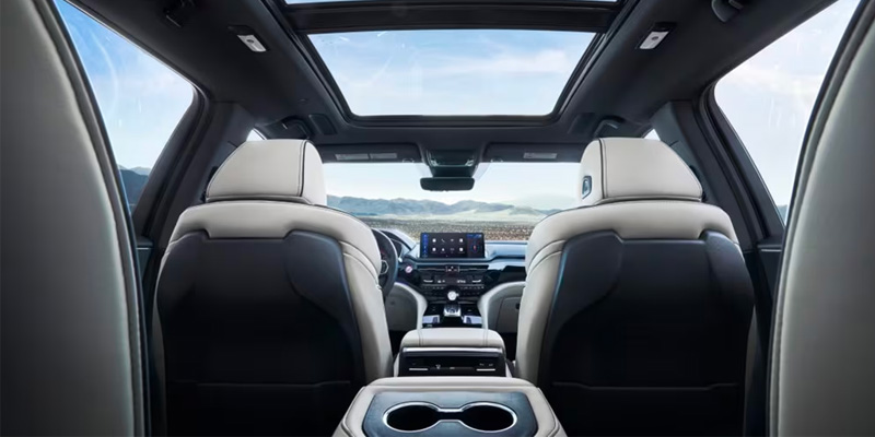 Interior view of a modern 2025 Acura MDX car showing leather seats, front console, and a sunroof with mountains in the background.